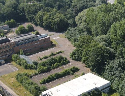 Luftaufnahme eines ungenutzten Parkplatzes und angrenzenden Bäumen.